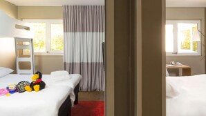A hotel room with two beds, a red carpet, a window with curtains, a desk with a lamp, and a stuffed toy on the left bed. - Ibis Caen Porte d Angleterre (Herouville-Saint-Clair)