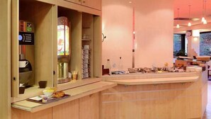 A modern kitchen with wooden cabinets, a coffee machine, and a counter with various items. - Ibis Caen Porte d Angleterre (Herouville-Saint-Clair)
