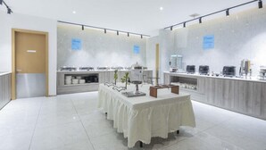 A modern, well-lit room with a central table covered with a white cloth, surrounded by various food dispensers and containers. - Holiday Inn Express Shangqiu Ancient Town (Shangqiu)