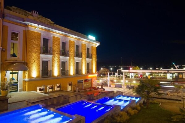 A hotel with a pool area, outdoor seating, and a well-lit facade at night. - Hotel Alize Evian (Evian-les-Bains)
