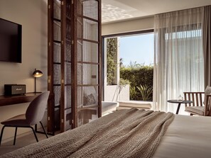 A modern hotel room with a large bed, a desk with a lamp, a chair, and a view of greenery through the window. - Contessina Suites & Spa - Adults Only (Zakynthos)