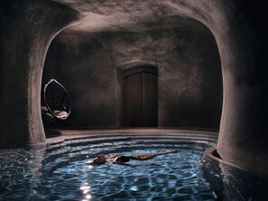 A spa pool with a person swimming, a hanging chair, and a door in a stone-walled room. - Contessina Suites & Spa - Adults Only (Zakynthos)