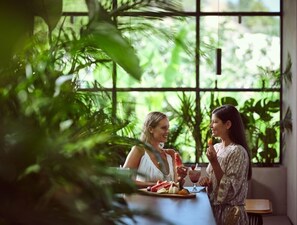 Two people at a table with a fruit platter and drinks, surrounded by large windows and greenery. - Contessina Suites & Spa - Adults Only (Zakynthos)