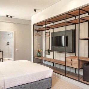 A modern bedroom with a bed, a TV mounted on a wooden and metal shelving unit, and a shower area.