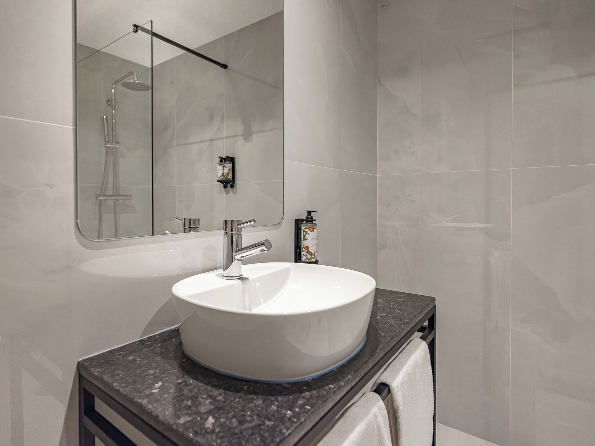 A modern bathroom with a white sink, a handheld showerhead, and a towel rack.