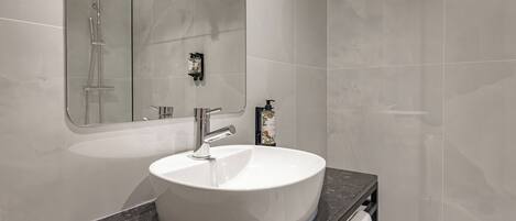 A modern bathroom with a white sink, a handheld showerhead, and a towel rack.