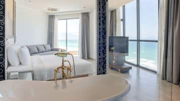 A modern hotel room with a large bathtub, a sofa bed, a television, and a view of the ocean.