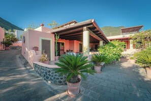 A pink building with a covered patio, potted plants, and a stone wall. - Residence Hotel Residence Hotel Al Belvedere Salina (Leni)