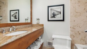 Un baño con lavamanos de encimera de granito, tocador de madera, inodoro blanco y dos fotografías en blanco y negro enmarcadas en la pared.