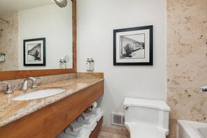 A bathroom with a granite countertop sink, a wooden vanity, a white toilet, and two framed black-and-white photographs on the wall. - Salishan Coastal Lodge (Gleneden Beach)