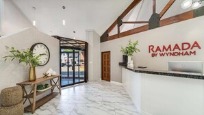 A reception area with a marble floor, a wooden bench, a clock, and a reception desk with a laptop. - Ramada by Wyndham Richfield UT I-70 (Richfield)
