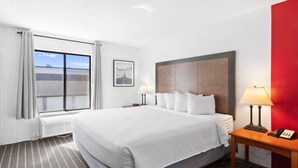 A hotel room with a large bed, two bedside tables with lamps, a window with curtains, a framed picture on the wall, and a red accent wall. - Ramada by Wyndham Richfield UT I-70 (Richfield)