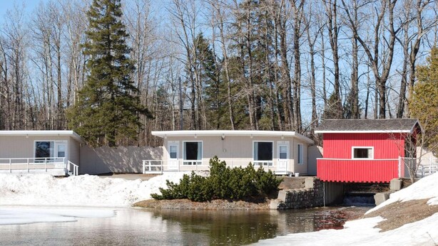 A lakeside cabin with a dock, a red shed, and a white building with a balcony. - Rodeway Inn Grand Falls (St. Andre)