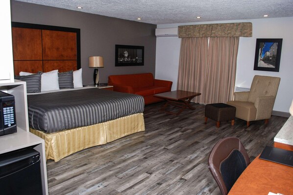 Een hotelkamer met een bed, rode bank, houten salontafel, stoel en bureau met een computer.