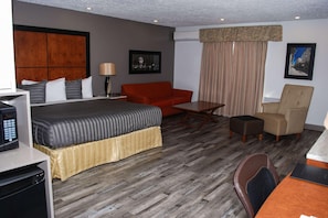 Una habitación de hotel con una cama, un sofá rojo, una mesa de centro de madera, una silla y un escritorio con un ordenador.