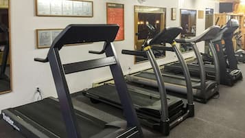 Un gimnasio con cintas de correr, equipo de ejercicio y carteles informativos en las paredes.