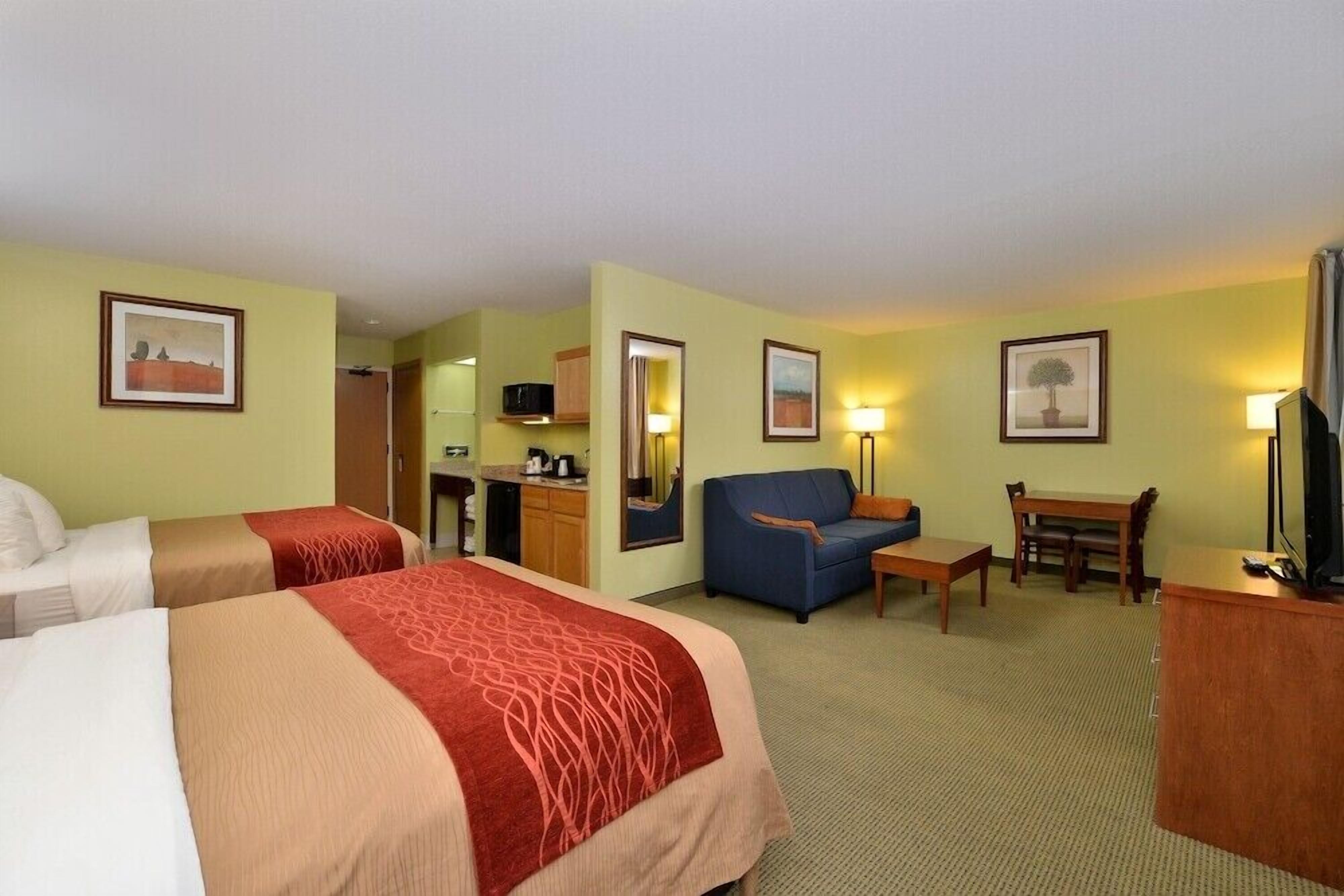 Quarto de hotel com duas camas, um sofá, uma escrivaninha, uma televisão e uma mesa de jantar.