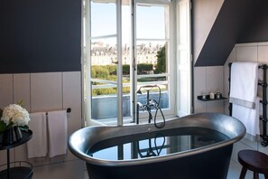 A modern bathroom with a freestanding bathtub, a window with a view of buildings, and a towel rack. - Cour des Vosges (Paris)