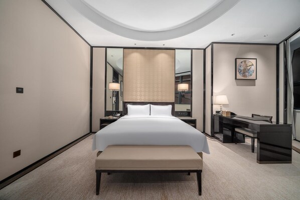 A hotel room with a large bed, a desk, a chair, and a mirror.