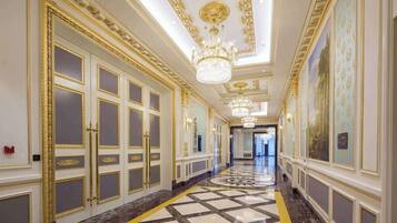 A grand hallway with ornate gold detailing, large doors, and a patterned floor.
