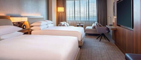 A hotel room with two large beds, a desk, a chair, a TV, and a large window with curtains.