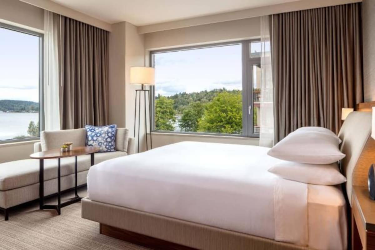A hotel room with a large bed, a sofa, a small table, and a view of a lake.