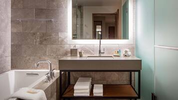 A modern bathroom with a bathtub, a large mirror, a vanity with a sink, and a shelf with towels.