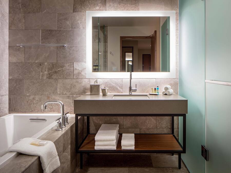 A modern bathroom with a bathtub, a large mirror, a vanity with a sink, and a shelf with towels.