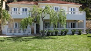 Un edificio de dos pisos con un balcón, un césped bien cuidado y un árbol en la fachada.