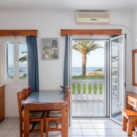 Una habitación con una mesa y sillas de madera, un cuadro y vista al mar a través de una puerta de cristal.