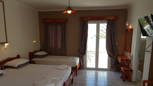 Habitación de hotel con dos camas, televisión, escritorio y puerta corredera de vidrio que da a un espacio al aire libre.