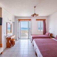 A hotel room with a balcony, a desk with a telephone, two beds with pink bedding, and a ceiling fan.
