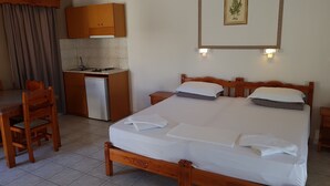Una habitación de hotel con una cama de madera, una kitchenette pequeña, una mesa de comedor y una cortina.