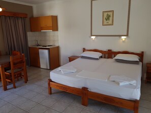 A hotel room with a wooden bed, a small kitchenette, a dining table, and a curtain. - Marina Bay Hotel Aparthotel (Kefalonia)
