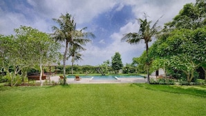 A well-maintained lawn with a swimming pool, surrounded by palm trees and lush greenery. - Kutus Kutus Ketewel Villa (Sukawati)