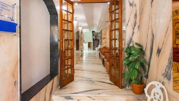 Um corredor com chão de mármore e portas de madeira que dão para uma área de estar.