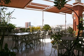 Une terrasse extérieure avec des tables et des chaises, entourée de plantes et offrant une vue sur le paysage urbain.