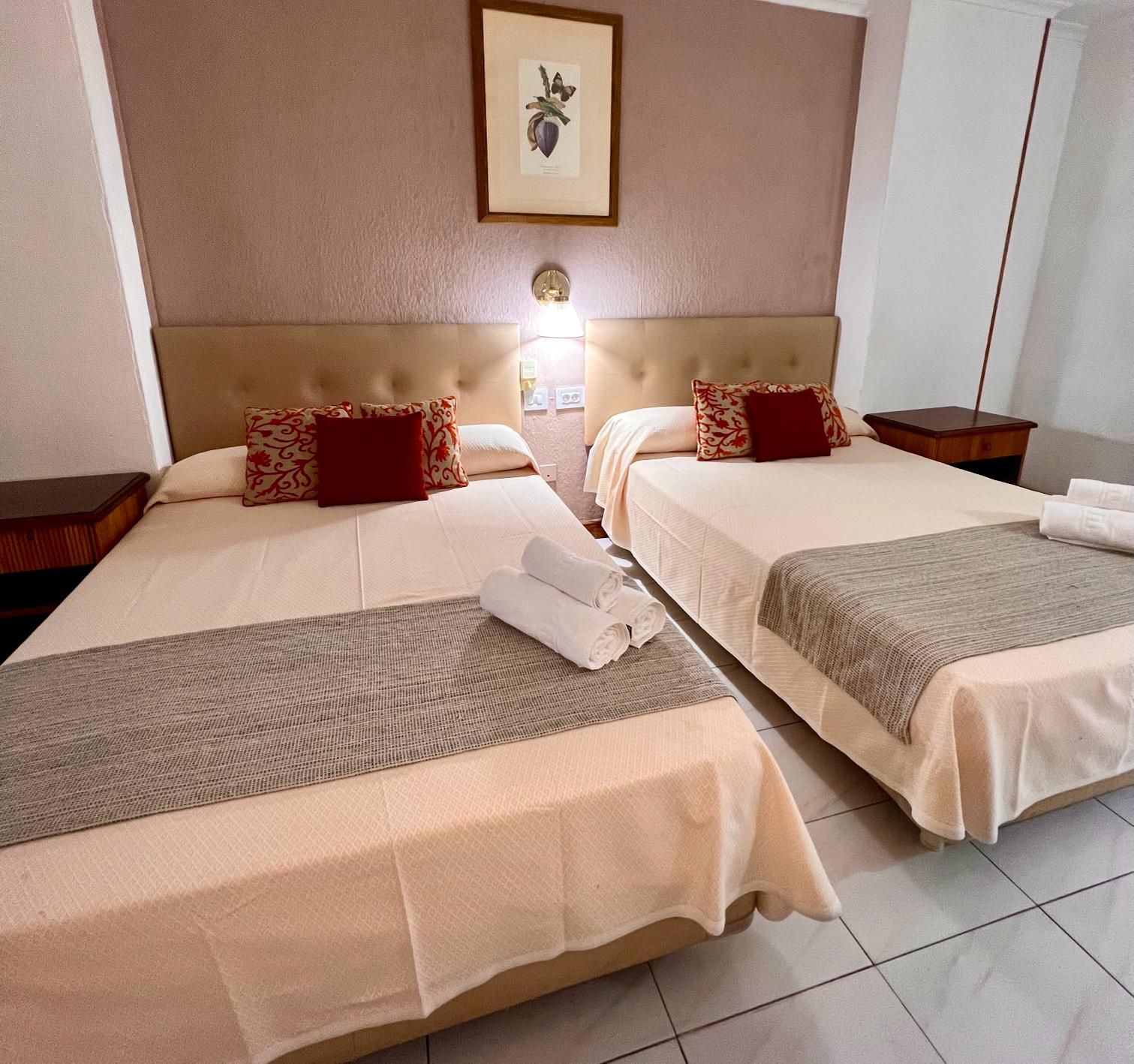 A hotel room with two beds, each with a headboard, a bedside table, and a wall-mounted light.