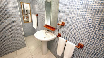 Un baño con lavamanos blanco, espejo y paredes con azulejos.
