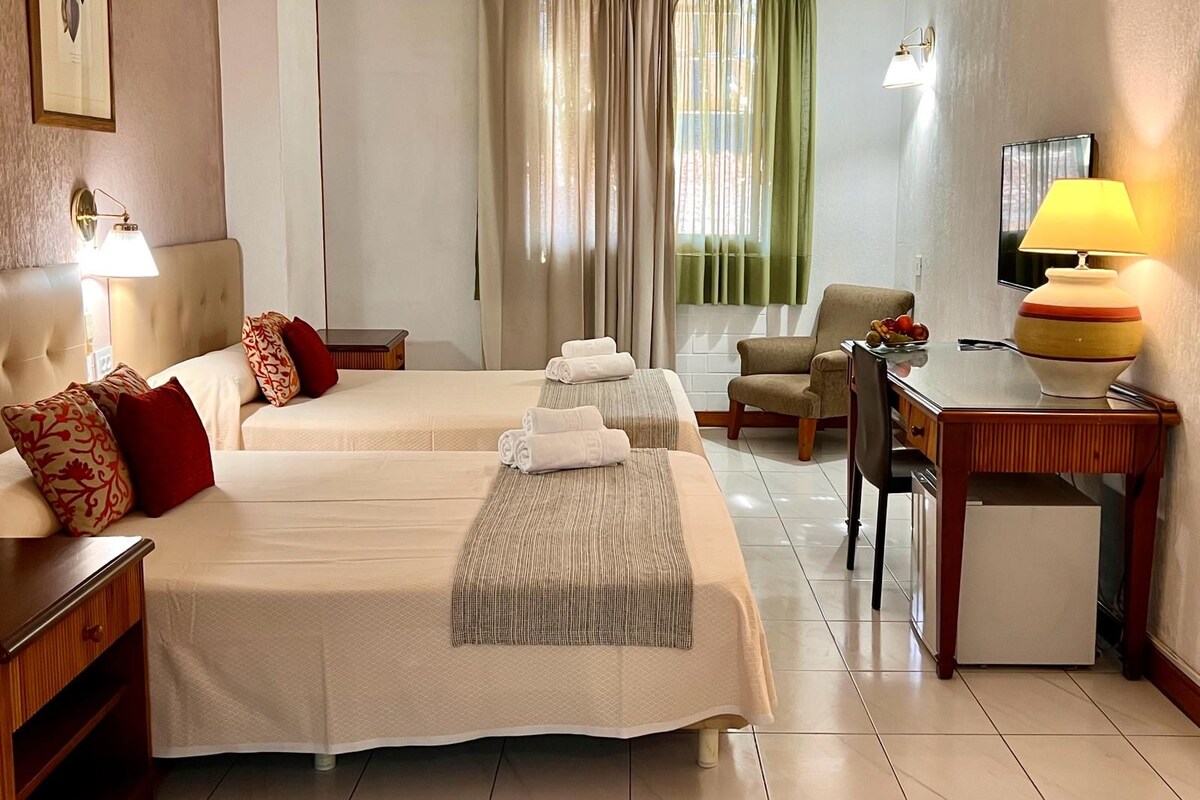 Ein Hotelzimmer mit zwei Betten, einem Schreibtisch, einem Sessel, einem Fernseher und einer Lampe.