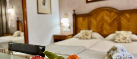 A hotel room with a bed, a bedside table with towels, a fruit bowl, and a painting on the wall.