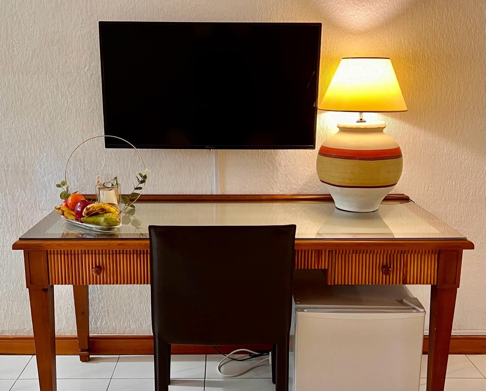 Un escritorio de madera con un televisor, una lámpara y un frutero.