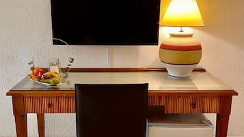 Un escritorio de madera con un televisor, una lámpara y un frutero.