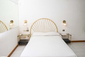 Ein Hotelzimmer mit einem Einzelbett, zwei Nachttischen, einem Spiegel und Wandleuchten.