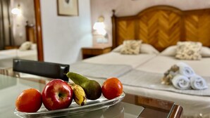 Habitación de hotel con cama, mesita de noche con toallas, frutero y un cuadro en la pared.