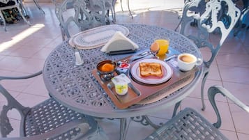 Una mesa redonda de metal con una bandeja de alimentos para el desayuno, como tostadas, huevos y jugo, rodeada de sillas de metal decorativas.