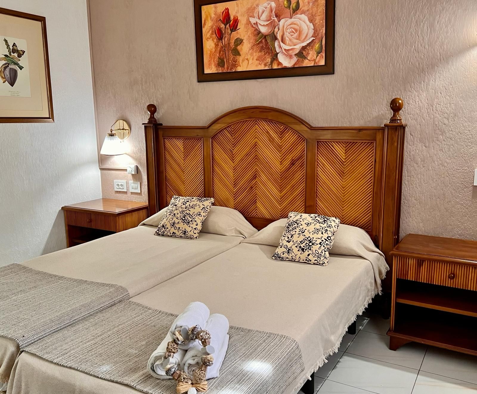 A double bed with a wooden headboard, two pillows, a bedside table with a lamp, and a framed botanical print on the wall.