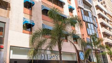 A hotel with multiple balconies, a storefront with a visible sign, and palm trees in the foreground.