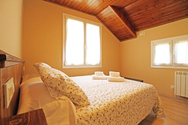 Un dormitorio con cama, dos ventanas, un radiador y vigas de madera en el techo.