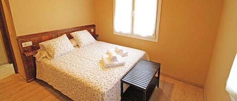 A bedroom with a wooden bed, a small bench, and a window with blinds.